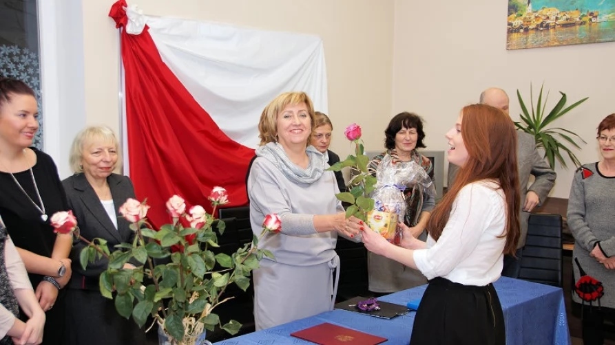 Pani Dyrektor Mari Wasiewicz-Galińska wręcza świadectwo ukończenia Liceum oraz dyplom za bardzo dobre wyniki w nauce słuchaczce Michalinie Grabowskiej. W tle Pani Dyrektor Zarządzająca Eliza Wasiewicz-Pawlaczyk wraz z gronem pedagogicznym